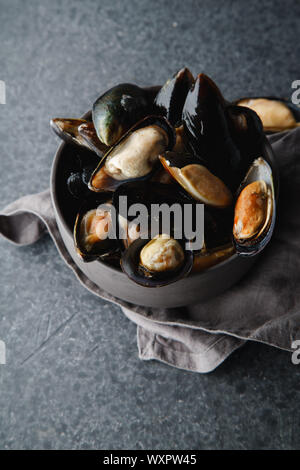 Les moules fraîches dans Bol en céramique noire sur fond de béton foncé Banque D'Images