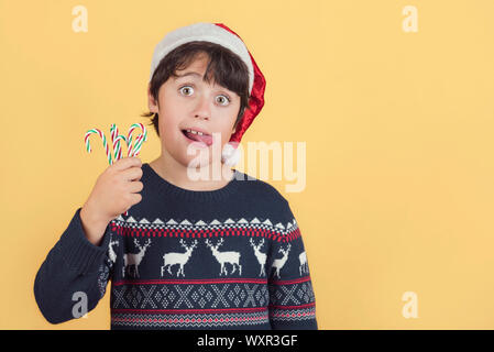 Child Wearing Christmas Santa Claus Hat et des cannes de bonbon sur fond jaune Banque D'Images