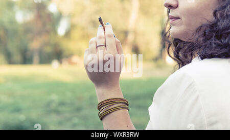 Le jeune fumeur de marijuana médicale à l'extérieur. conjointe La jeune femme fumer du cannabis blunt, close-up. Le cannabis est un concept d'alternative de fines herbes Banque D'Images