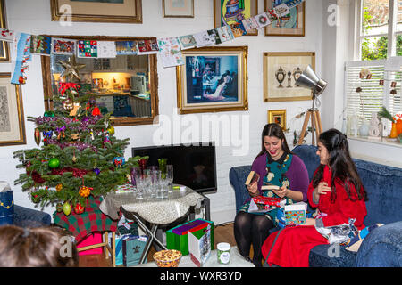 Deux jeunes femmes ouvrant des cadeaux de Noël à côté de l'arbre décoré à la maison à Londres, souriant pendant la célébration festive du matin. Londres, Angleterre, Royaume-Uni Banque D'Images
