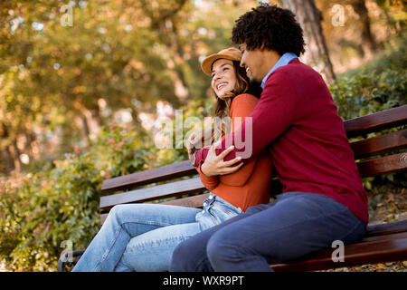 Multiratial jeune couple d'amoureux assis sur un banc dans le parc de la ville d'automne Banque D'Images