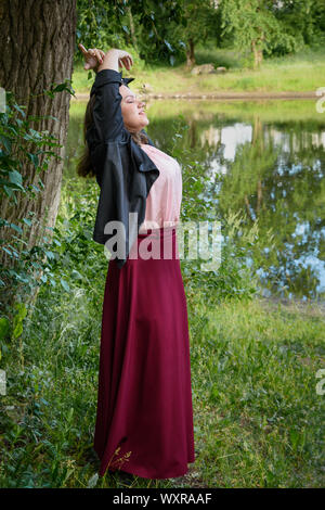 Fille brune est de danser dans le parc. Jeune fille en noir veste et jupe rouge avec des cheveux longs en journée d'été. Modèle de taille plus Banque D'Images