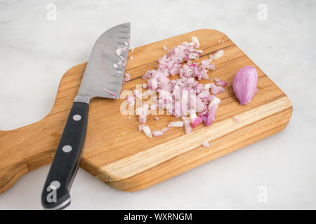 Échalote hachée sur une planche à découper en bois : une échalote hachée avec toute une gousse sur une planche à découper en bois avec un couteau de cuisine. Banque D'Images