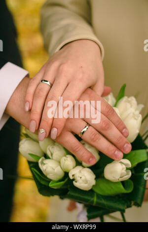 Les mains des mariés avec des bagues de fiançailles en argent sur le bouquet de mariée de tulipes blanches. Concept de mariage d'automne. Banque D'Images