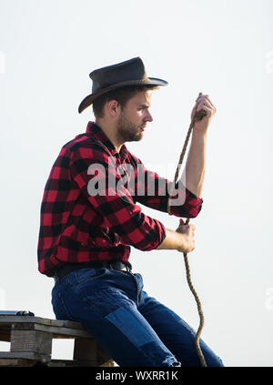 La vie au ranch. Cowboy avec lasso corde fond de ciel. Agriculteur réfléchie réflexion sur l'entreprise. Ranch travailleur. Eco farm. Concept de l'agriculture. Bel homme en chapeau et costume de style rustique. Garder ranch. Banque D'Images