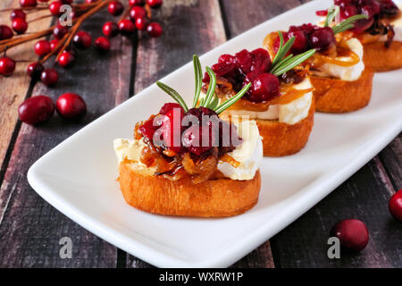 Crostini aux canneberges, hors-d'oignons caramélisés et de brie. Gros plan sur une assiette de service contre un arrière-plan en bois. Banque D'Images