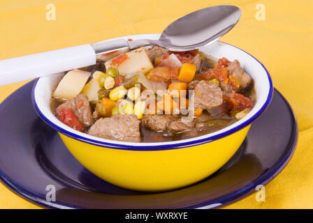 Soupe de légumes et boeuf fait maison servi dans un bol en étain jaune avec une cuillère reposant sur le bol. Banque D'Images