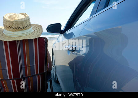 Dame en chaise à côté de voiture à une plage Banque D'Images
