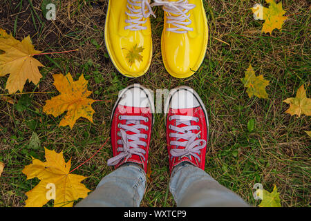 Bottes en caoutchouc jaune et rouge sale vieux sneakers avec jaune feuilles d'érable sur une pelouse humide Banque D'Images