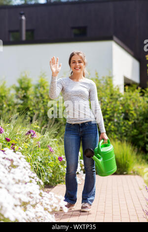 Le jardinage et les gens heureux concept - jeune femme avec fleurs et arrosoir en agitant la main dans son jardin d'été Banque D'Images