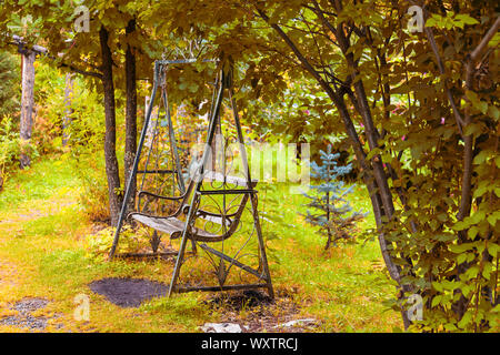 Un vieux fer forgé metal retro swing avec un banc en bois dans un style vintage se trouve dans un jardin ou dans un parc pour les enfants, divertissement, détente et d Banque D'Images