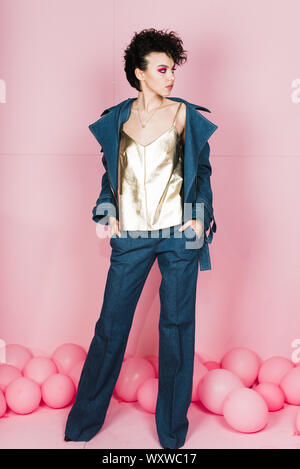 Une fille avec un grand sourire sincère est en studio sur un fond rose pastel. Une fille avec une étrange coiffure et maquillage lumineux volant. Banque D'Images