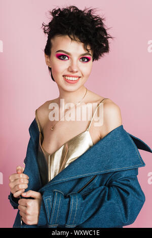 Une fille avec un grand sourire sincère est en studio sur un fond rose pastel. Une fille avec une étrange coiffure et maquillage lumineux volant Banque D'Images