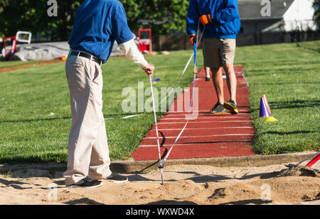 Deux représentants d'athlétisme sont une mesure de temps ou distance triple saut lors d'une compétition à l'extérieur sur une journée ensoleillée. Banque D'Images