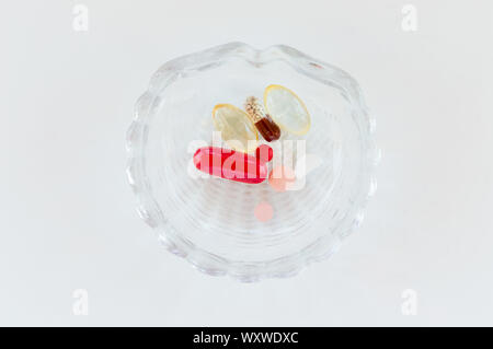 Vue de dessus de plusieurs comprimés médicaux dans un petit bol en verre sur fond blanc. Concept de médicaments. Banque D'Images
