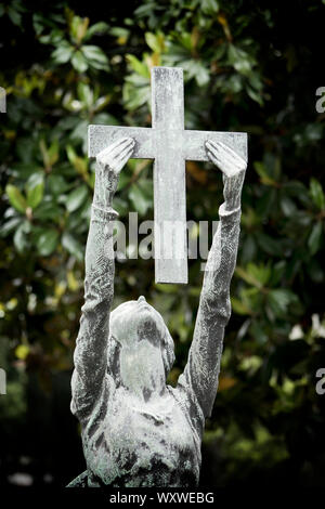 Ancienne statue avec croix sur une tombe dans le Cimitero Monumentale (cimetière monumental), l'un des deux plus grands cimetières de Milan Banque D'Images