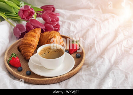 Petit-déjeuner au lit avec café, croissants et des fraises avec des tulipes roses sur fond. Banque D'Images