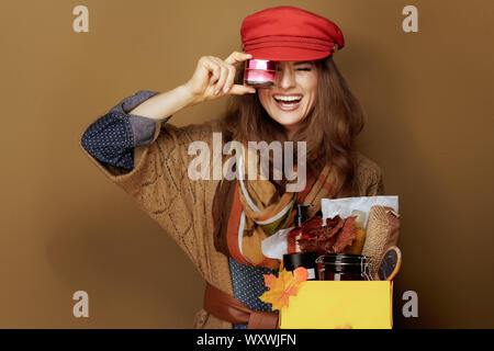 De 40 ans à la mode smiling woman in red cap, foulard, chemise et veste en jeans montrant l'automne beauté cosmétiques fort et crème visage isolé sur ba beige Banque D'Images