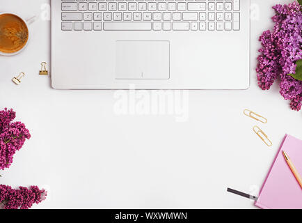 Concept de poste de travail féminin moderne. Ordinateur portable, de café, de belles fleurs violettes et roses bloc-notes sur le tableau blanc, vue du dessus. Banque D'Images