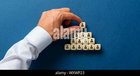 Homme de main en bois d'empilage de dés avec personne d'icônes sur eux dans une forme de pyramides dans une image conceptuelle d'hiérarchie. Sur fond bleu marine. Banque D'Images