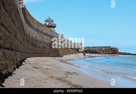 Le redoutable mur de Smeaton's Pier à St Ives vu du dessous à marée basse, avec une figure solitaire marchant le long de la plage Banque D'Images