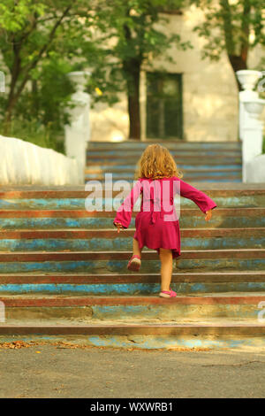 Un bébé fille en robe rose d'atteindre le haut de l'escalier ancien bleu vintage Banque D'Images