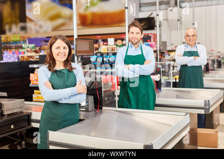 Trois vendeurs de tablier vert au supermarché caissière avec bras croisés Banque D'Images