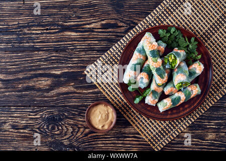 Rouleaux de printemps d'Asie brut de papier de riz aux crevettes, nouilles de riz, de laitue et de menthe sur une plaque de faïence plombages sur un tapis de table en bambou, vue d'abo Banque D'Images