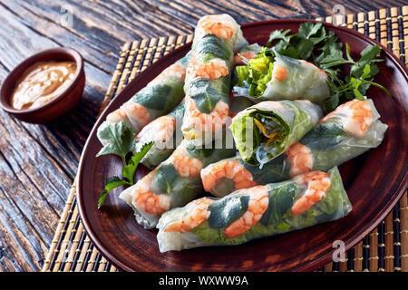 Rouleaux de printemps d'Asie brut de papier de riz aux crevettes, nouilles de riz, de laitue et de menthe sur une plaque de faïence plombages sur un tapis de table en bambou, vue d'abo Banque D'Images