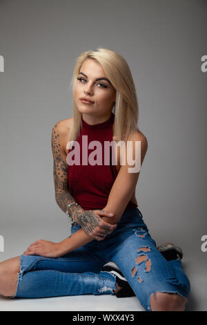 Une belle jeune femme avec des tatouages assis portant un body sans manches et arrache un jean bleu Photo Stock Alamy