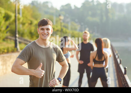 Guy sportive des sourires sur l'arrière-plan d'amis sportifs dans le parc Banque D'Images