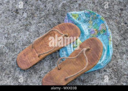 Hippy usés tongs & globe dégonflé sur surface en béton. Métaphore 250-504, télévision earthers, théories du complot, preuve de la terre plate, la pseudoscience Banque D'Images