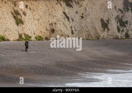 Un couple debout sur une plage de galets balayées par de la recherche à la grosses vagues et des tempêtes. Banque D'Images