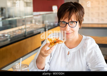 Femme de race blanche aux yeux verts, cheveux courts, lunettes de vue et de manger une pizza dans un restaurant. Banque D'Images