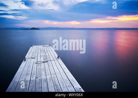 Une vieille jetée en bois pour les bateaux naviguant sur le lac de Bolsena à Capodimonte, sur l'eau, en face de l'île Bisentina, durant le lever du soleil avec des nuages colorés et su Banque D'Images