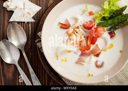 Soupe aux fruits de mer avec les calamars, les crevettes, le bacon, les légumes et les asperges sur table en bois Banque D'Images