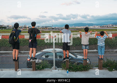 Cinq jeunes garçons regarder un avion de décoller de la clôture périphérique de l'Aéroport de Taipei Songshan, Taiwan Banque D'Images