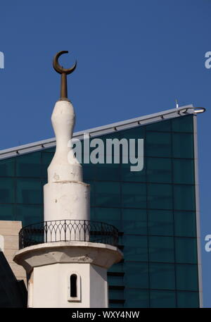 D'un minaret blanc une ancienne mosquée avec Crescent est en contraste à l'encontre de bâtiments en béton et verre moderne au centre-ville de Koweït City Banque D'Images