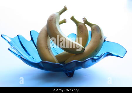 Seule la banane dans un bol en verre décoratif bleu turquoise contre fond blanc Banque D'Images