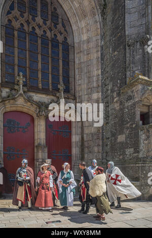 Un groupe de trois femmes dans la robe médiévale et cinq hommes en costumes croisés en dehors des grandes portes de l'église rouge à la fête médiévale de Guerand Banque D'Images