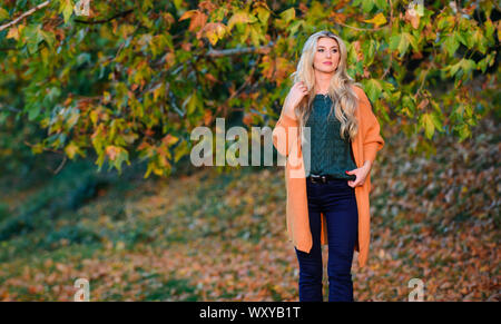 Tenue confortable. Adorable petite fille blonde posing in outfit chaleureux et cosy de l'automne nature fond flou. Création pour agréable fin de semaine. Femme à pied. La lumière au coucher du soleil Tenues décontractées confortable pour la fin de l'automne. Banque D'Images