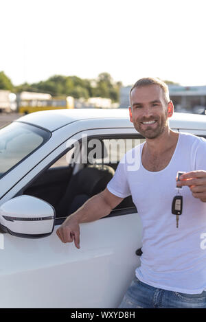 Un conducteur se trouve à proximité d'une voiture avec une clé dans sa main et sourit. Banque D'Images