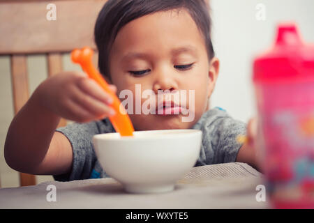 Un jeune garçon d'apprendre à manger de façon autonome avec une cuillère dans la main et de mâcher son repas. Banque D'Images