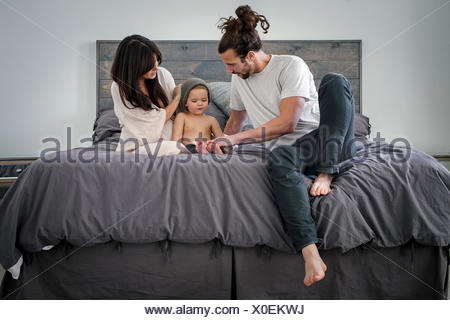 Un jeune couple et leur jeune fils, assis sur leur lit.