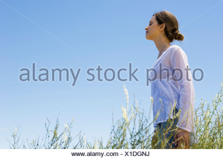 Jeune femme debout dans l'herbe haute, les yeux fermés, side view