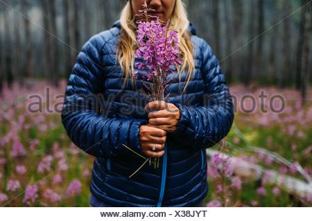 Portrait of mid adult woman holding manteau rembourré fleurs sauvages, le lac Moraine, Banff National Park, Alberta Canada