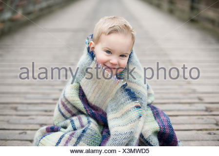 Portrait d'un garçon enveloppé dans une couverture, assis sur un pont en bois