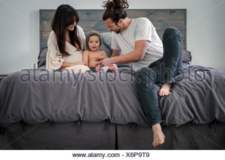 Un jeune couple et leur jeune fils, assis sur leur lit.