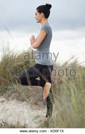 Femme mature en posture de l'arbre sur la plage, vue latérale