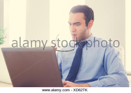 Fronçant man biting ses lunettes et à l'aide d'un laptop sitting on a sofa